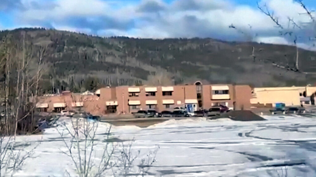 Tumbler Ridge Secondary School seen from afar, a brown building against snow-covered ground and forested Rocky Mountain foothills